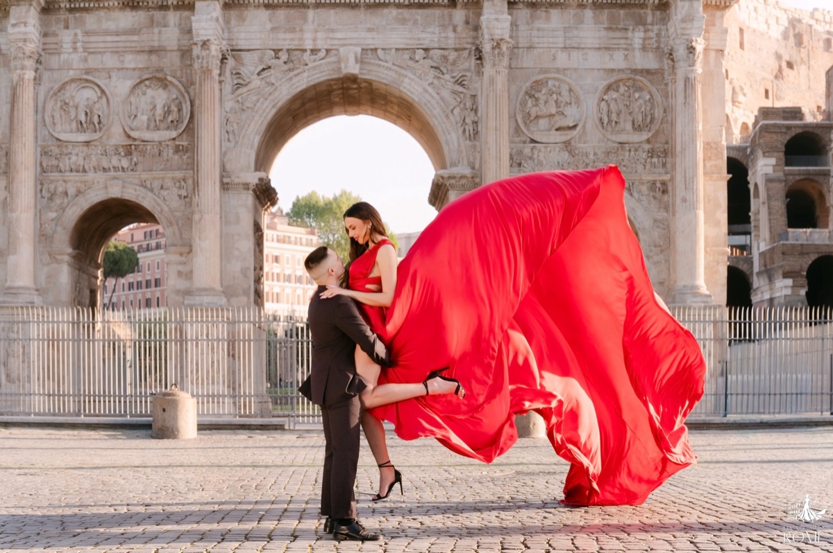 Couple flying dress pose The Dip: he leans her back while supporting her, red train flying, Arch of Constantine, Rome