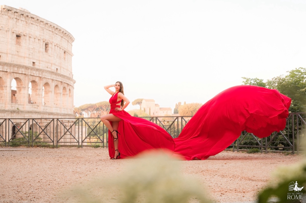 Flying dress pose The Icon: one hand in the hair and the red train drawing an arc, Colosseum at sunrise, Rome