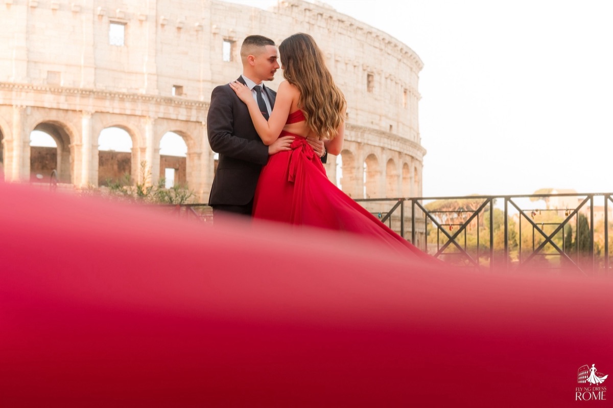 Couple flying dress pose The Tender Moment: forehead to forehead with the red fabric blurred in the foreground, Colosseum, Rome