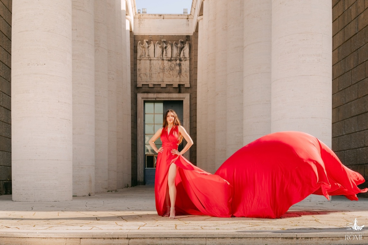 Flying dress pose The Reveal: facing the camera, hands on hips, five meters of red train opened out on the ground, EUR Planetarium, Rome